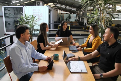 equipo de trabajo vm global group compuesto por tres mujeres y dos hombre, sentados en una mesa de madera realizando una reunión laboral