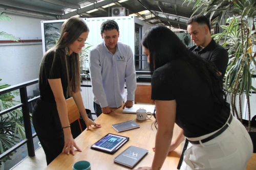 cinco personas del equipo de trabajo de vm global reunidos en una mesa de madera mirando estadistas empresariales en una tablet